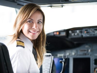 Portrait of a happy pilot in the airplane's cockpit looking at the camera smiling before take off - travel concepts