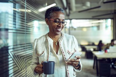 Close up of a senior businesswoman using a phone while having coffee in the office