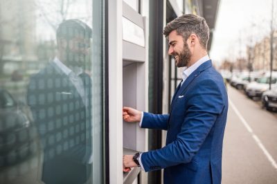 Photo of smiling mid adult businessman withdrawing money from a cash machine.